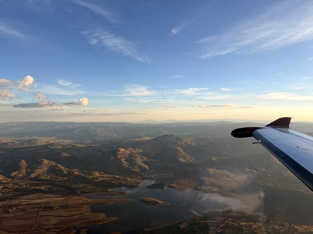 Golden-hour view past an aircraft wing over foothills and a reservoir